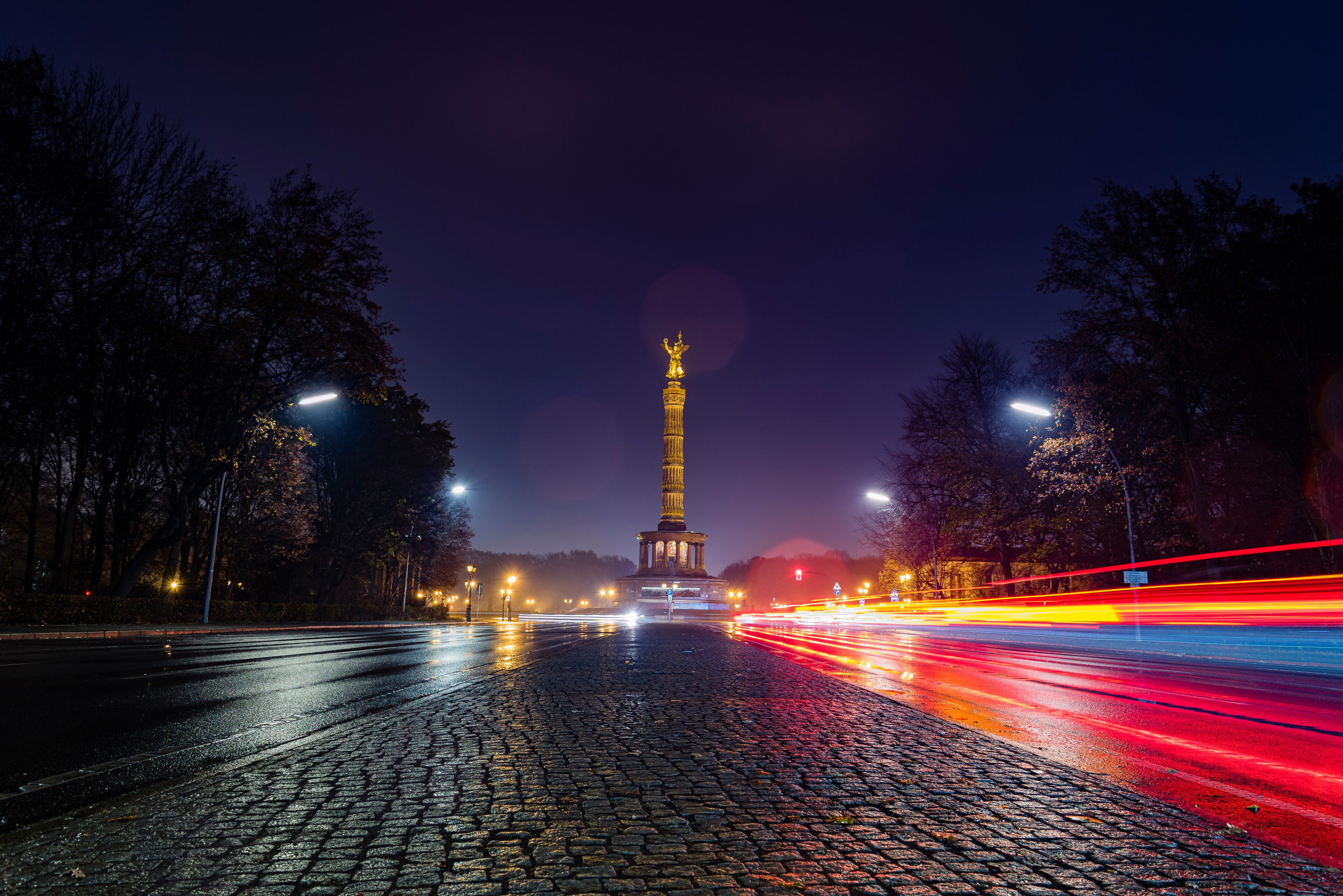 Siegessäule in Berlin bei Nacht, umgeben von Lichtern vorbeifahrender Autos