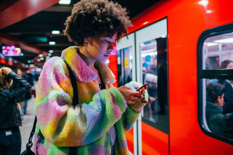 Junge Frau mit Smartphone wartet abends in U-Bahn-Station