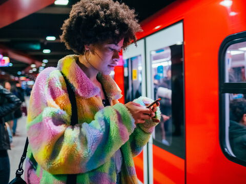 Junge Frau mit Smartphone wartet abends in U-Bahn-Station